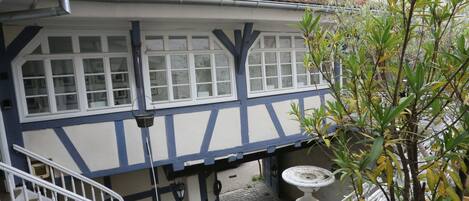 Un edificio tradicional con entramado de madera, con una escalera visible y un pequeño espacio exterior con un bebedero para pájaros.