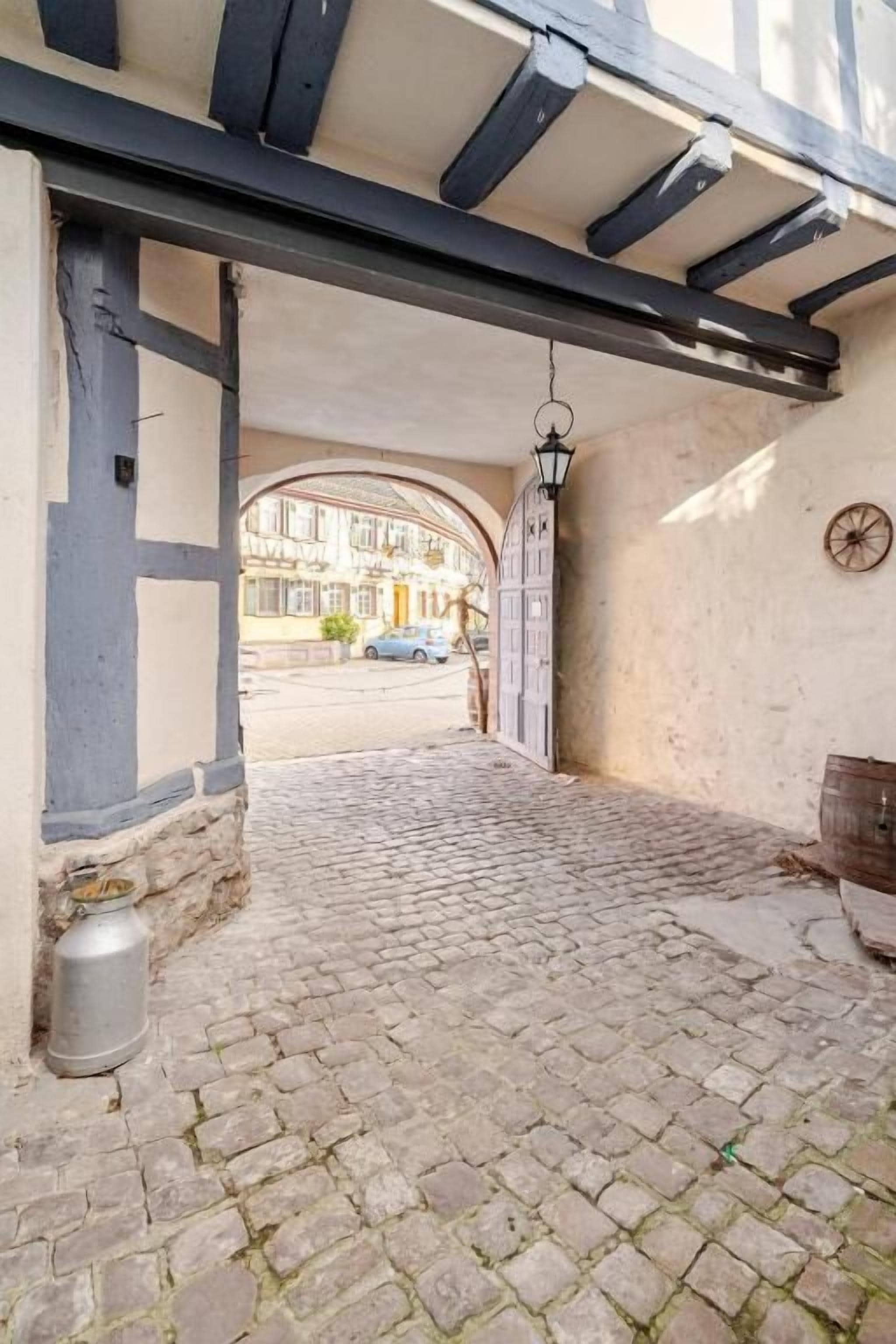 A cobblestone entrance with a wooden archway, a metal lantern, and a rustic wooden barrel.