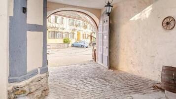 A cobblestone entrance with a wooden archway, a metal lantern, and a rustic wooden barrel.