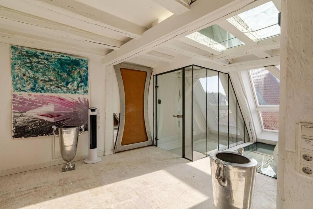 A modern interior with a glass door leading to a balcony, a large abstract painting, and a metallic object on the floor.