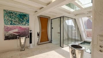 A modern interior with a glass door leading to a balcony, a large abstract painting, and a metallic object on the floor.