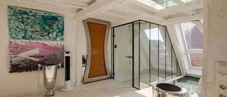 Een modern interieur met een glazen deur naar een balkon, een groot abstract schilderij en een metalen voorwerp op de vloer.