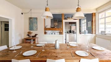 A dining area with a wooden table set for six, white chairs, and hanging pendant lights.