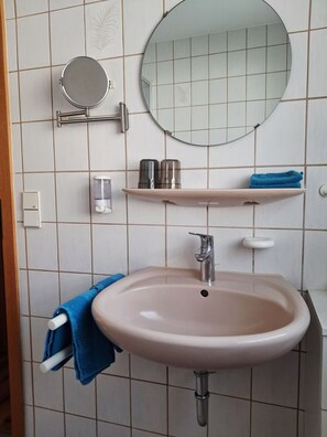 Ein Badezimmer mit Waschbecken, Spiegel, Handtuchhalter und Seifenspender.