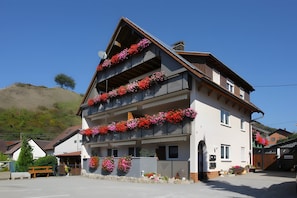 Ein mehrstöckiges Gebäude mit Blumen geschmückten Balkonen, einem klaren Himmel und einer hügeligen Landschaft im Hintergrund.