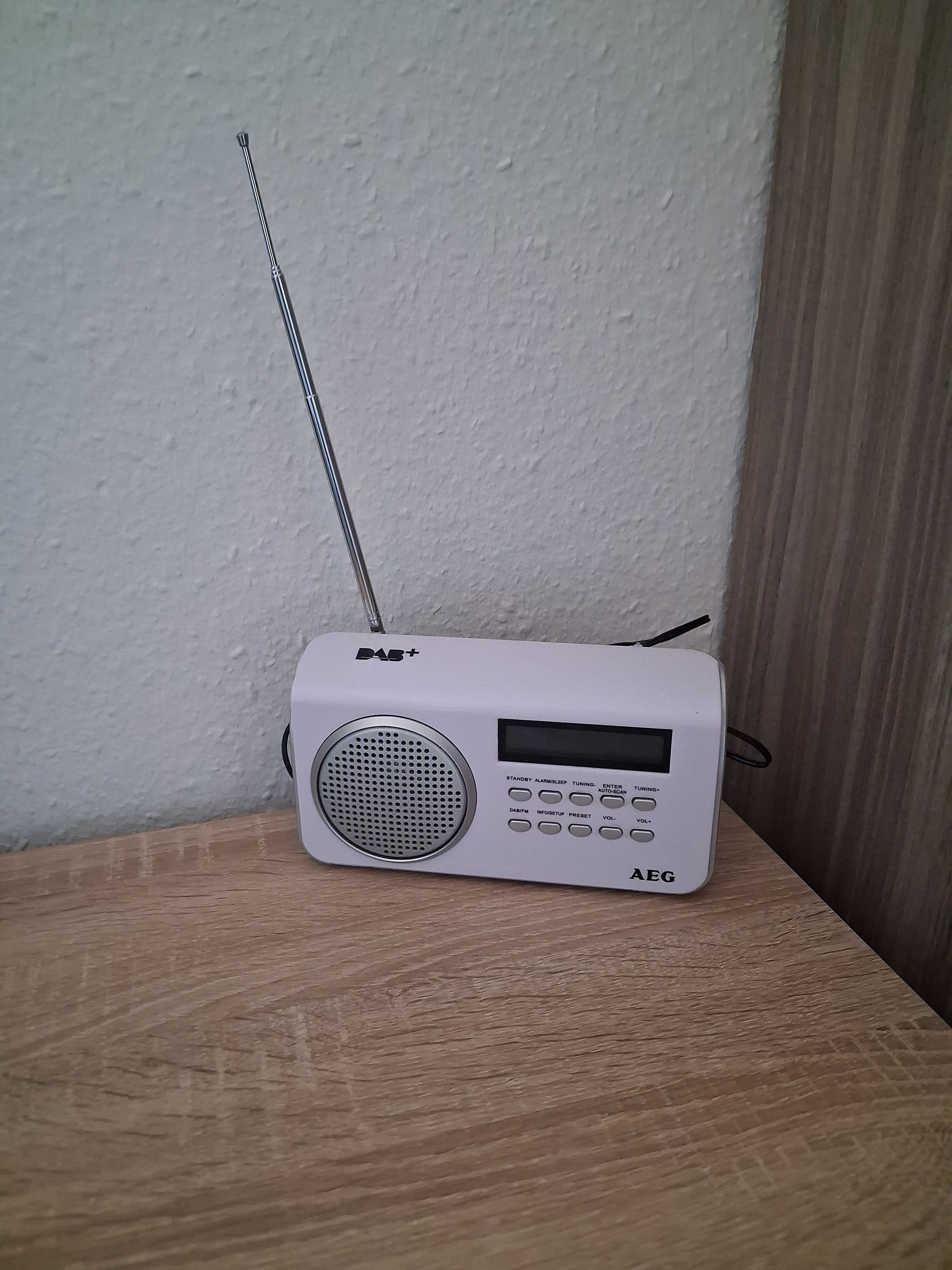 Een witte radio met speaker en antenne op een houten oppervlak voor een structuurwand.
