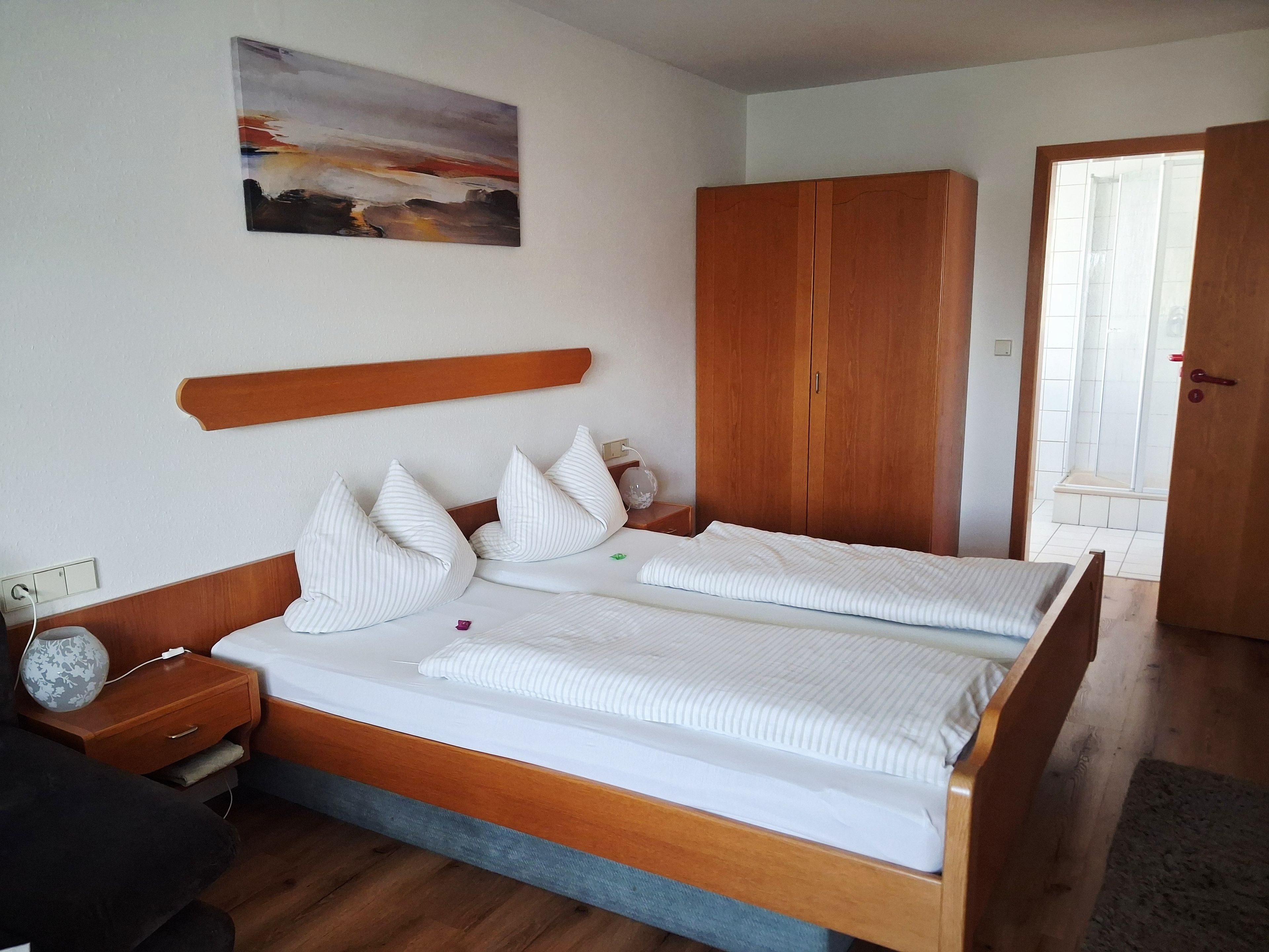 Ein Doppelbett mit Holz Kopfteil, ein Nachttisch mit Lampe und ein Kleiderschrank.