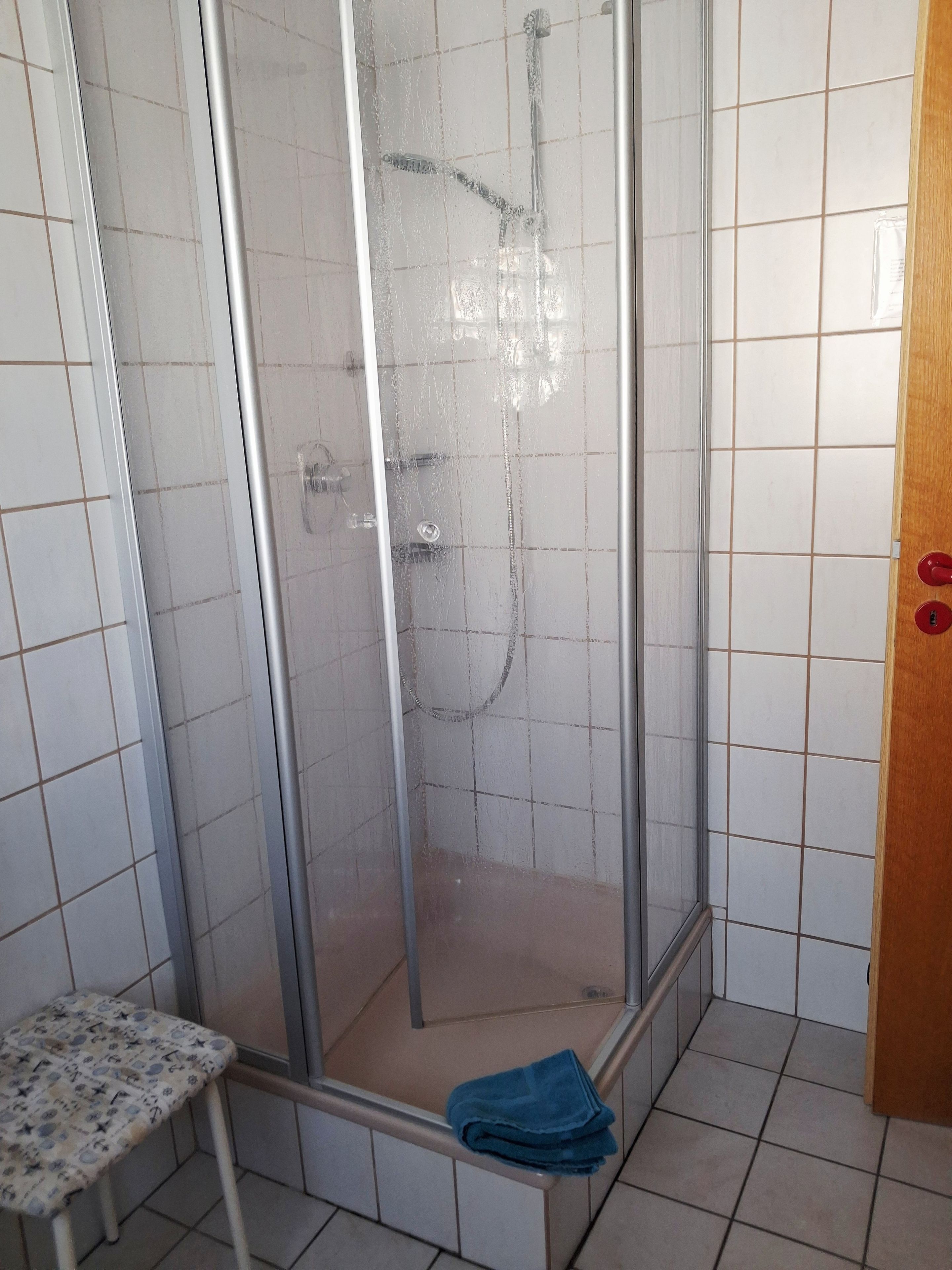 Eine Duschkabine mit Glastür, einer Sitzbank und einem Handtuch auf dem Boden.
