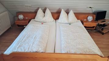 Uma cama de casal com duas almofadas, uma mesa de cabeceira com abajur e uma TV sobre um suporte.