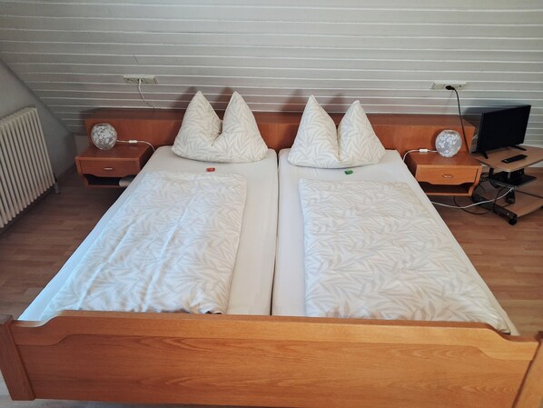 A double bed with two pillows, a bedside table with a lamp, and a TV on a stand.
