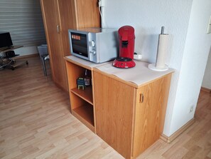 A kitchenette with a microwave, coffee maker, and a bottle of wine on a wooden cabinet.