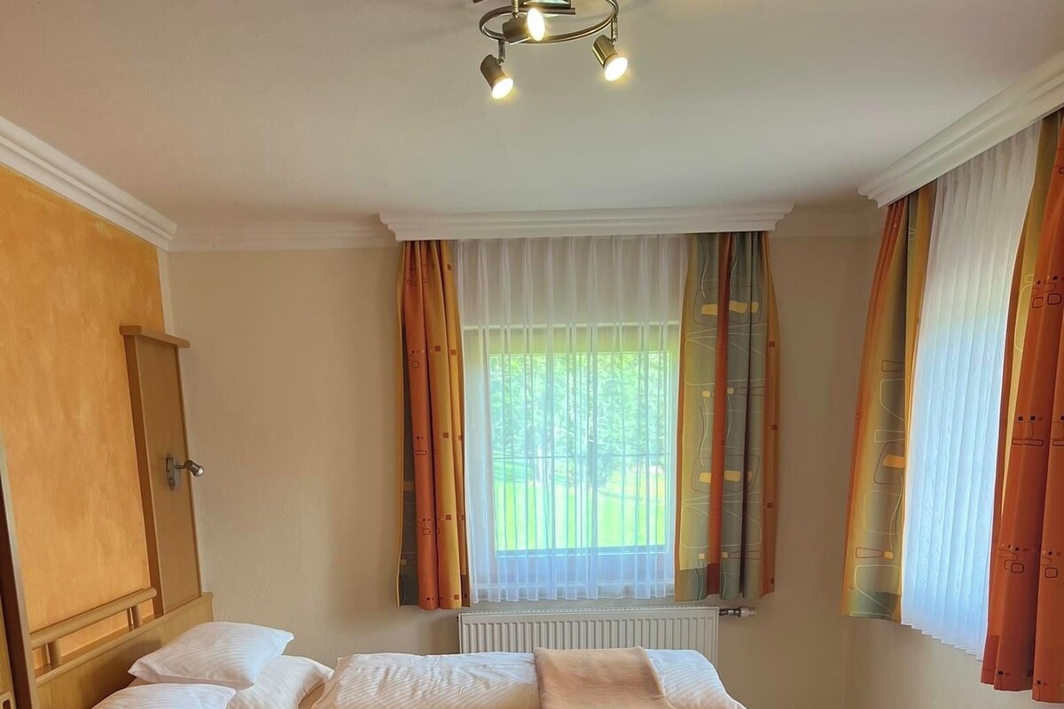 Ein Schlafzimmer mit Bett, einem Fenster mit Vorhängen, einer Heizung und einem gemusterten Teppich.
