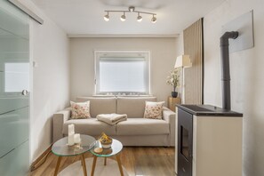 A compact living space with a sofa, a glass table, a fireplace, and a window with blinds.