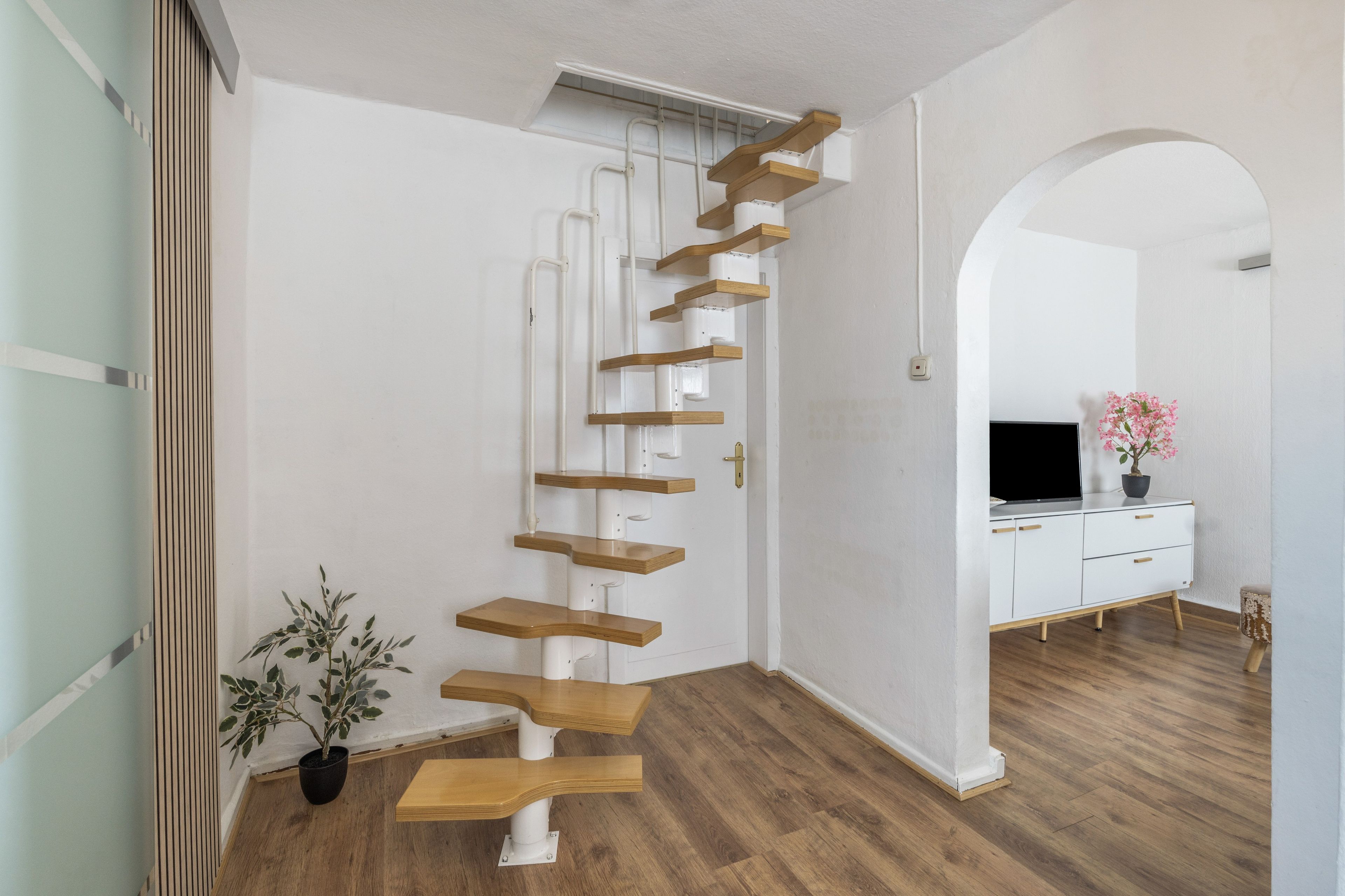A modern interior with a wooden staircase, a white cabinet, and a potted plant.