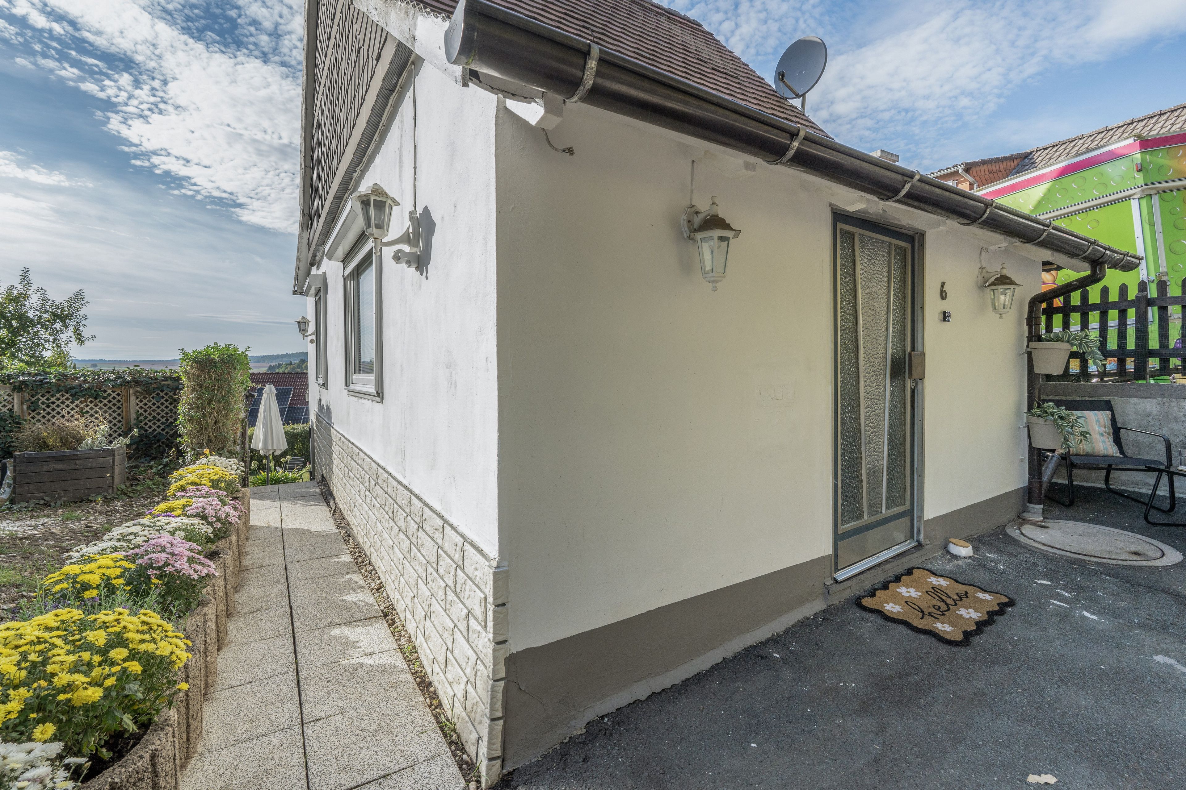 Ein Wohngebäude mit weißer Fassade, einer Tür mit Fensterteil und einer kleinen Veranda mit einer Bank.