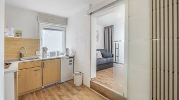 A compact kitchen with a built-in dishwasher, a sink, and a window with blinds.