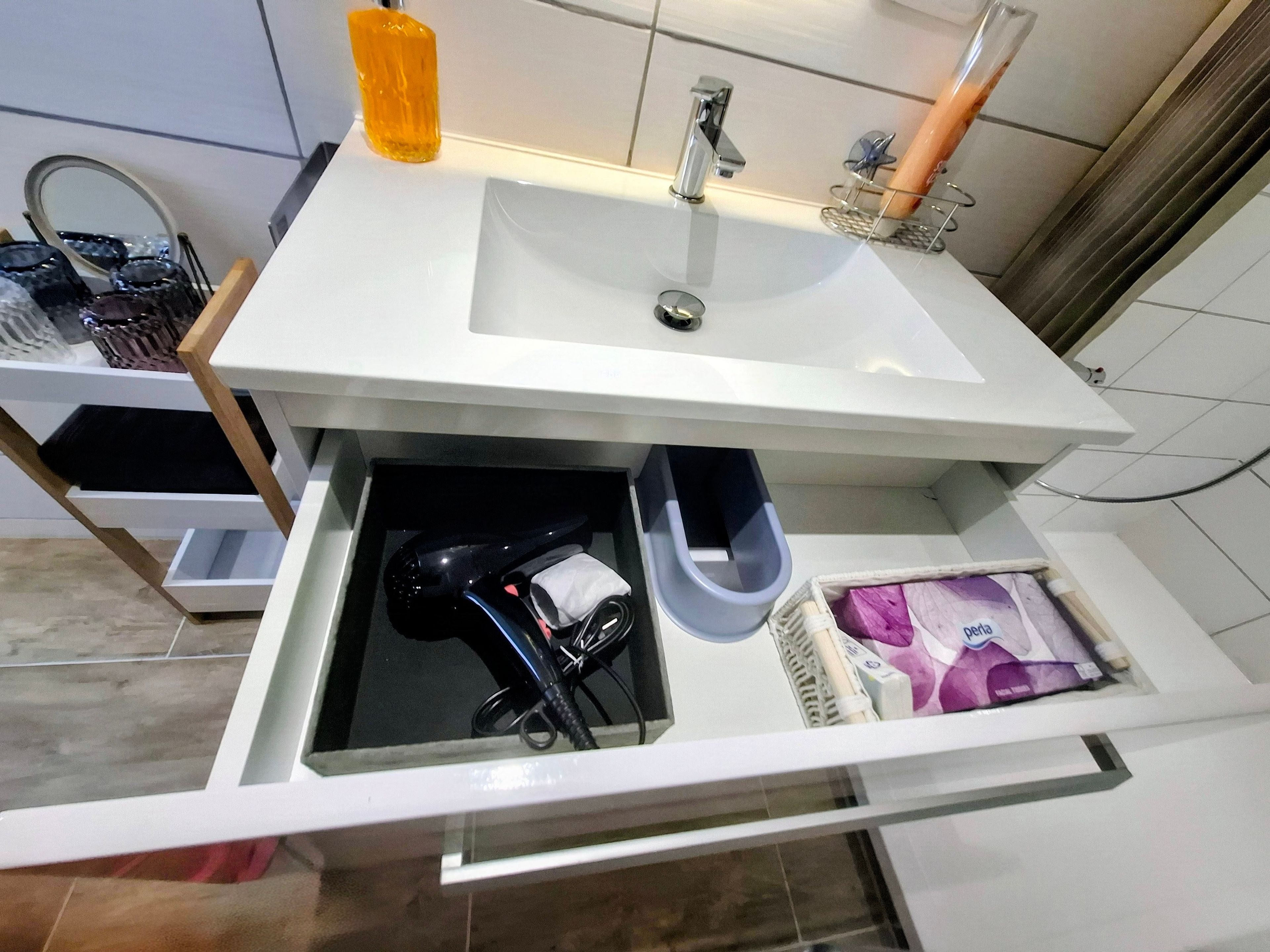 Ein Badezimmer mit einem weißen Waschbecken, einem Spiegel, einer Zahnbürstenhalterung und einer Aufbewahrungsbox.