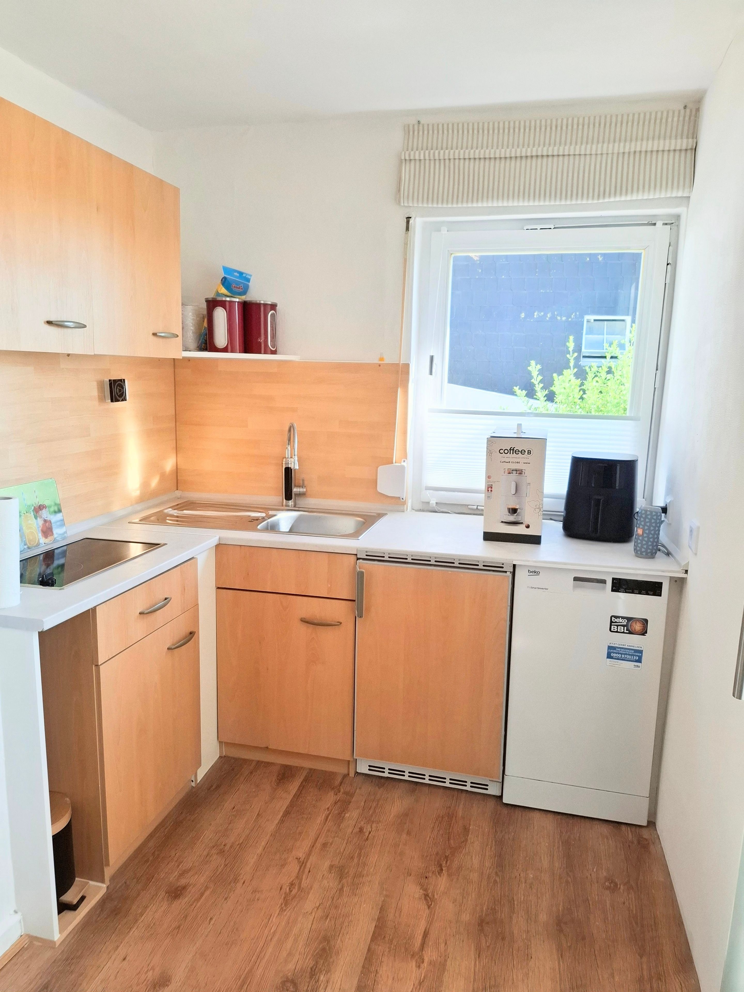 Eine kleine Küche mit Holzausstattung, einer Spüle, einem Geschirrspüler und einem Fenster mit Blick auf Grünflächen.