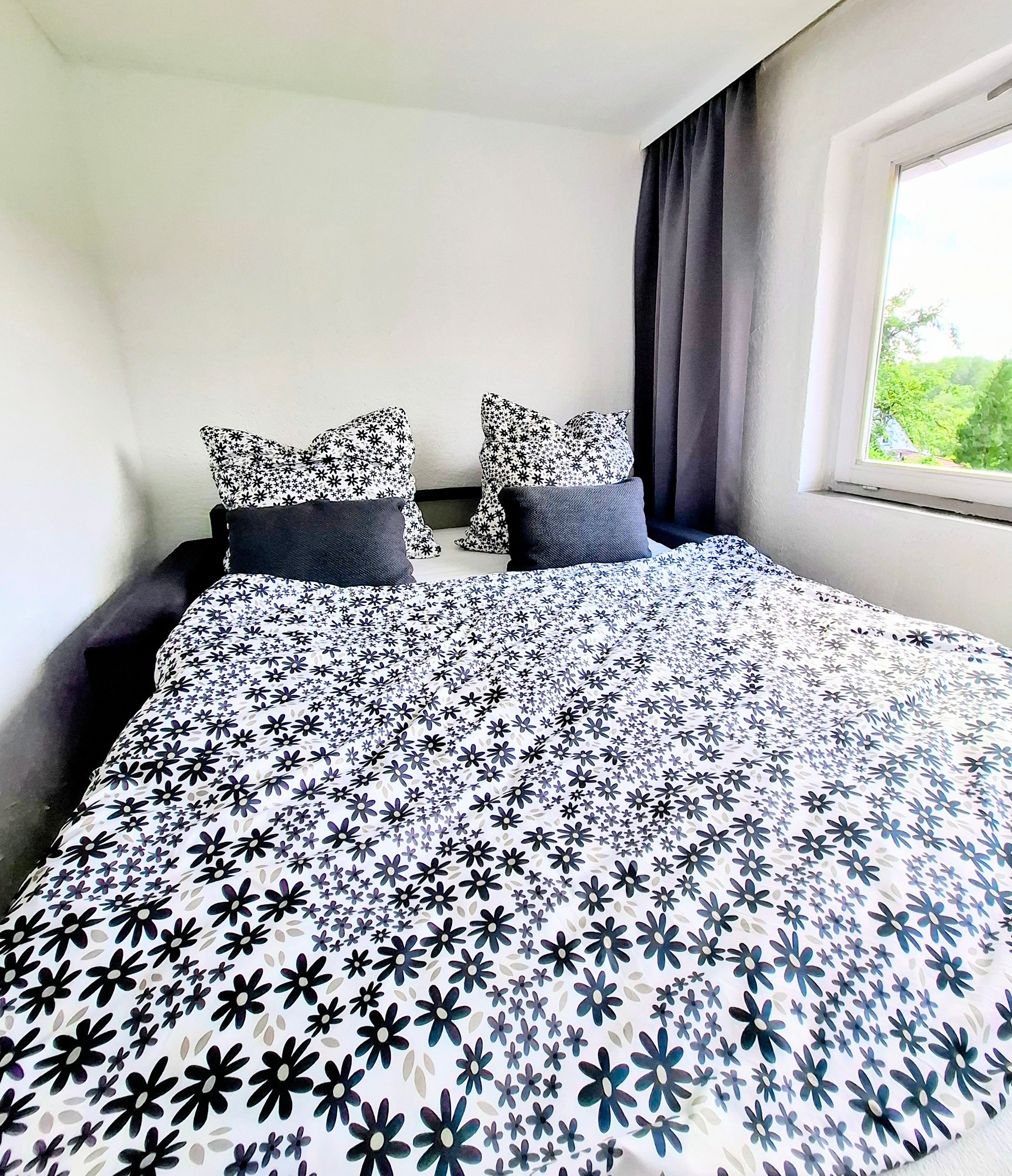 Une chambre à coucher avec un lit, deux oreillers, une fenêtre avec des rideaux et une vue sur la verdure à l’extérieur.