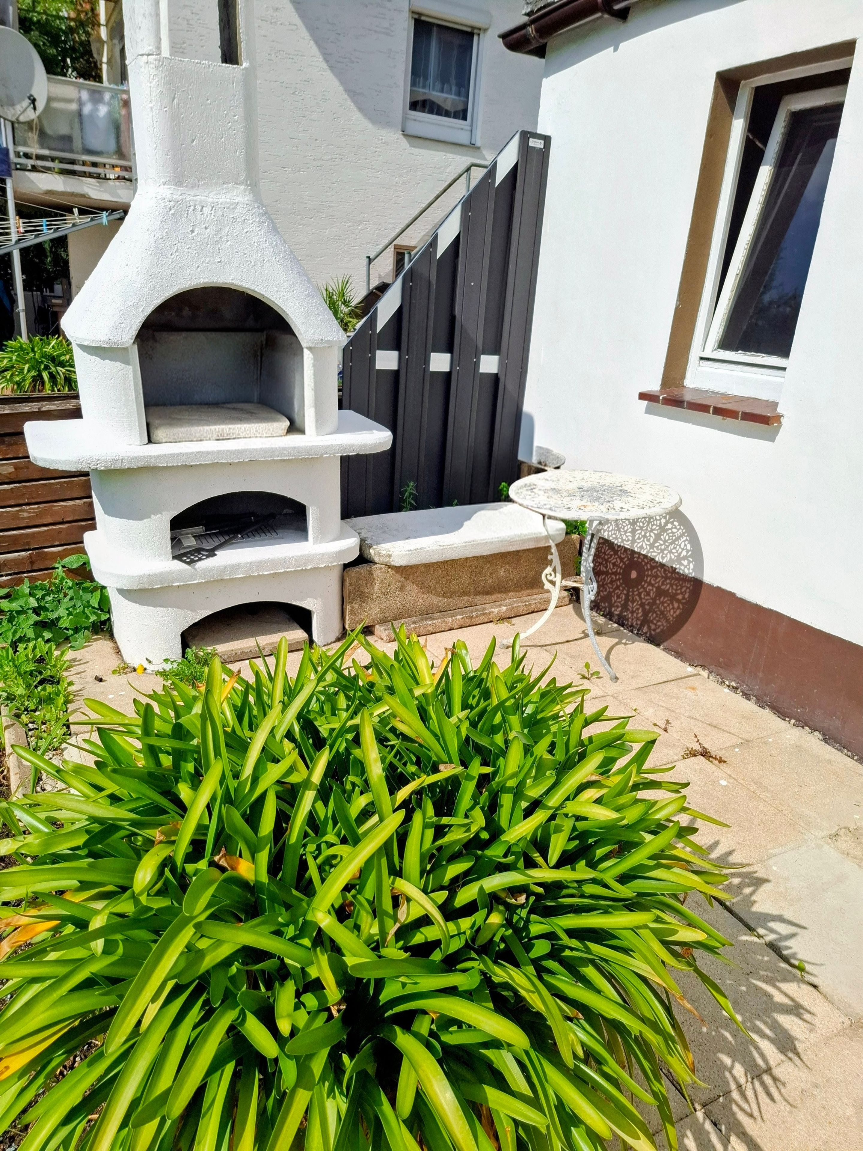 Ein Steinofen im Freien, ein kleiner Tisch und ein Blumentopf in einem Wohnambiente.