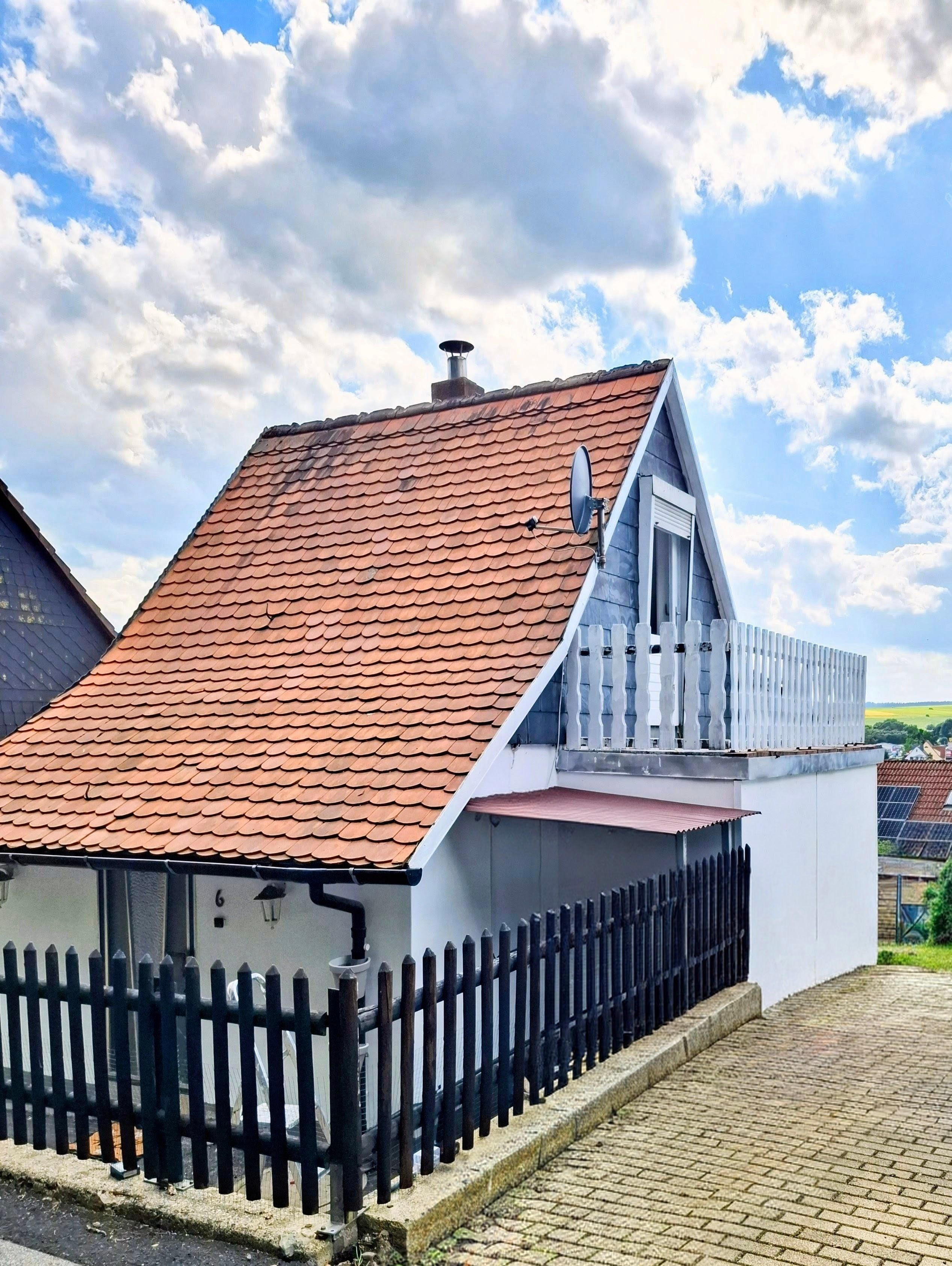 Une maison avec un toit recouvert de tuiles rouges, une façade blanche et une clôture noire.