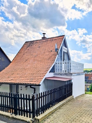 Une maison avec un toit recouvert de tuiles rouges, une façade blanche et une clôture noire.
