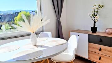 Un comedor moderno con una mesa redonda, sillas blancas, un jarrón con plantas secas y vistas al exterior.