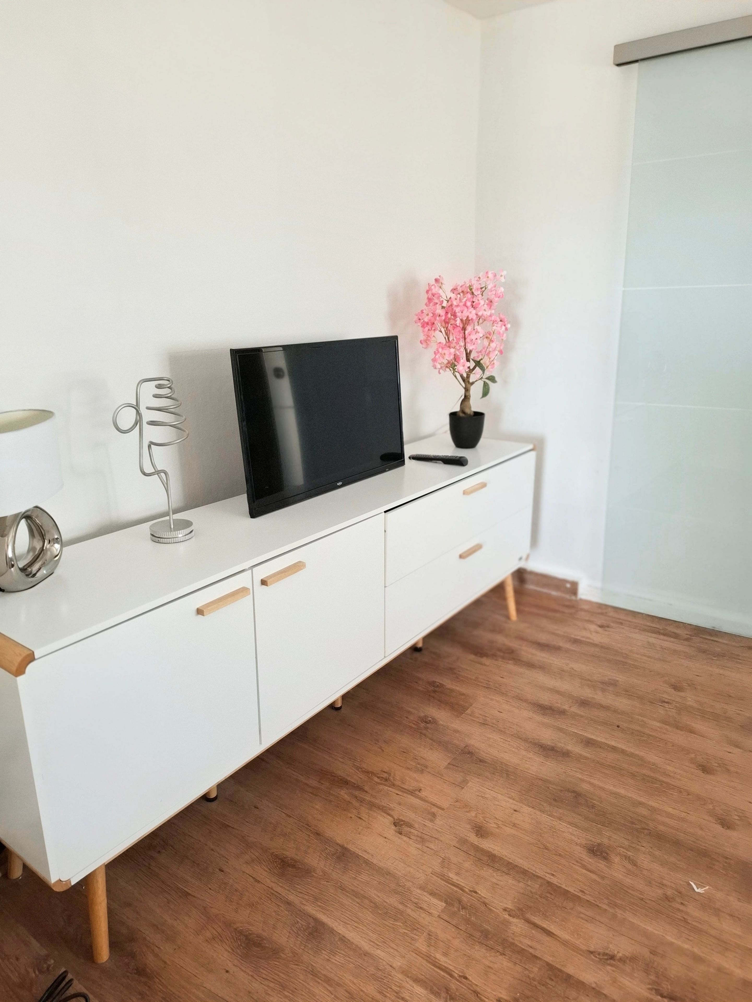 Ein weißes Fernsehregal mit einem Flachbildfernseher, einem Blumentopf und einer Fernbedienung.
