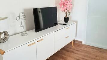 Un mueble blanco para televisor con un televisor de pantalla plana, una planta en maceta y un control remoto.