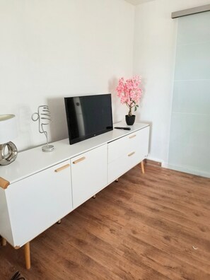 A white TV stand with a flat-screen TV, a potted plant, and a remote control.
