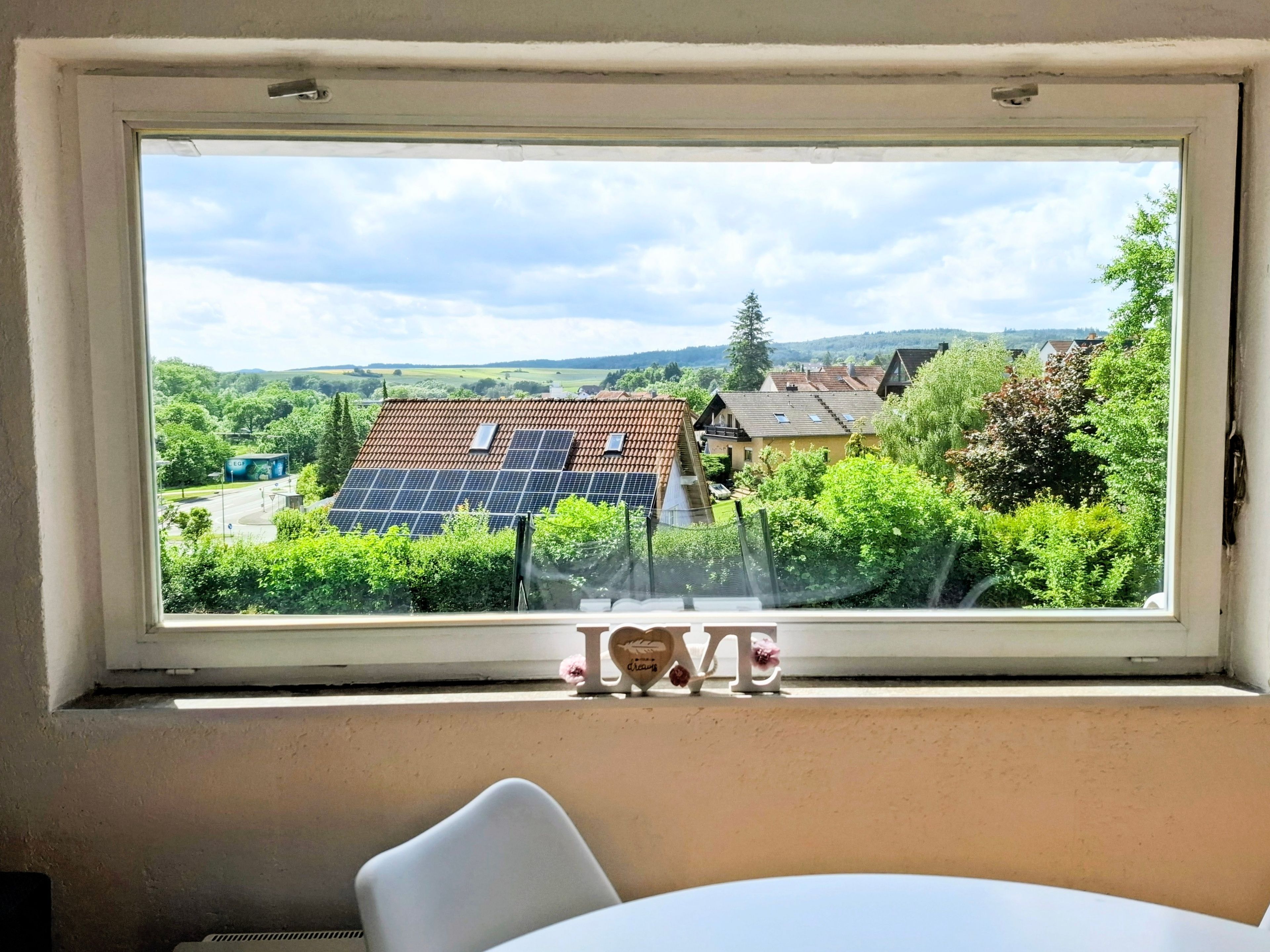 Une pièce avec une fenêtre donnant sur un quartier résidentiel, une table blanche et une chaise blanche.