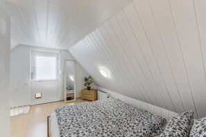 A bedroom with a sloped ceiling, a bed with a floral bedspread, a bedside table with a plant, and a door with a window.