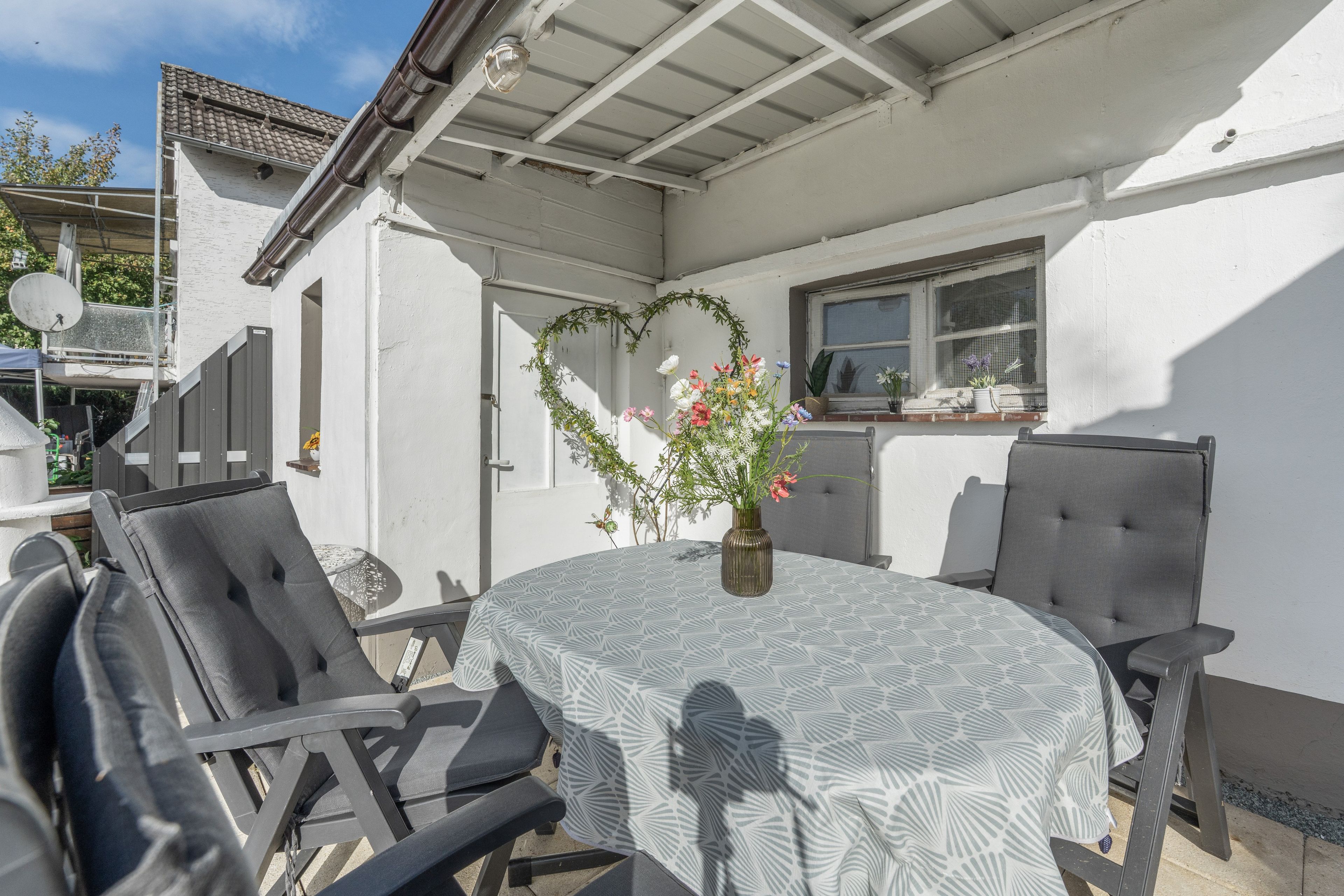 Eine Terrasse im Freien mit einem runden Tisch, zwei Stühlen und einer herzförmigen Blumenkomposition.