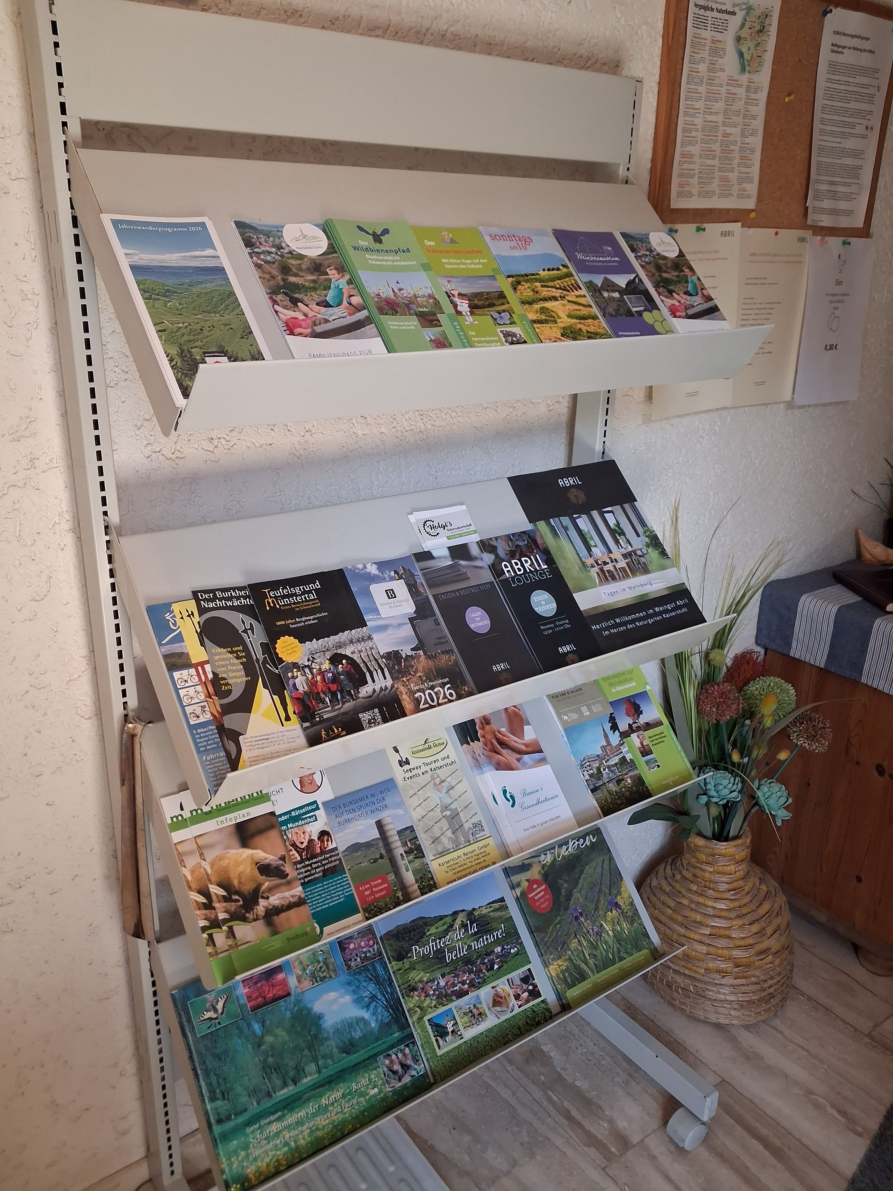 Exposição de folhetos informativos e brochuras em uma estante, com um mural de avisos ao fundo.