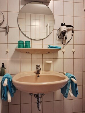 Ein Badezimmer mit Waschbecken, Spiegel, Handtuchhalter und einem an der Wand befestigten Föhn.