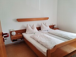 Ein Doppelbett mit Holz Kopfteil, zwei Nachttische mit Lampen und eine Steckdose an der Wand.