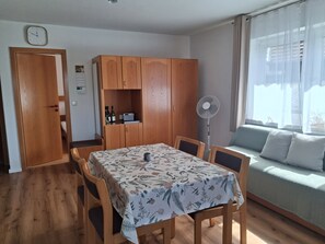 Ein Zimmer mit Esstisch, Stühlen, einer Couch, einem Holzschrank, einem Ventilator und einer Wanduhr.