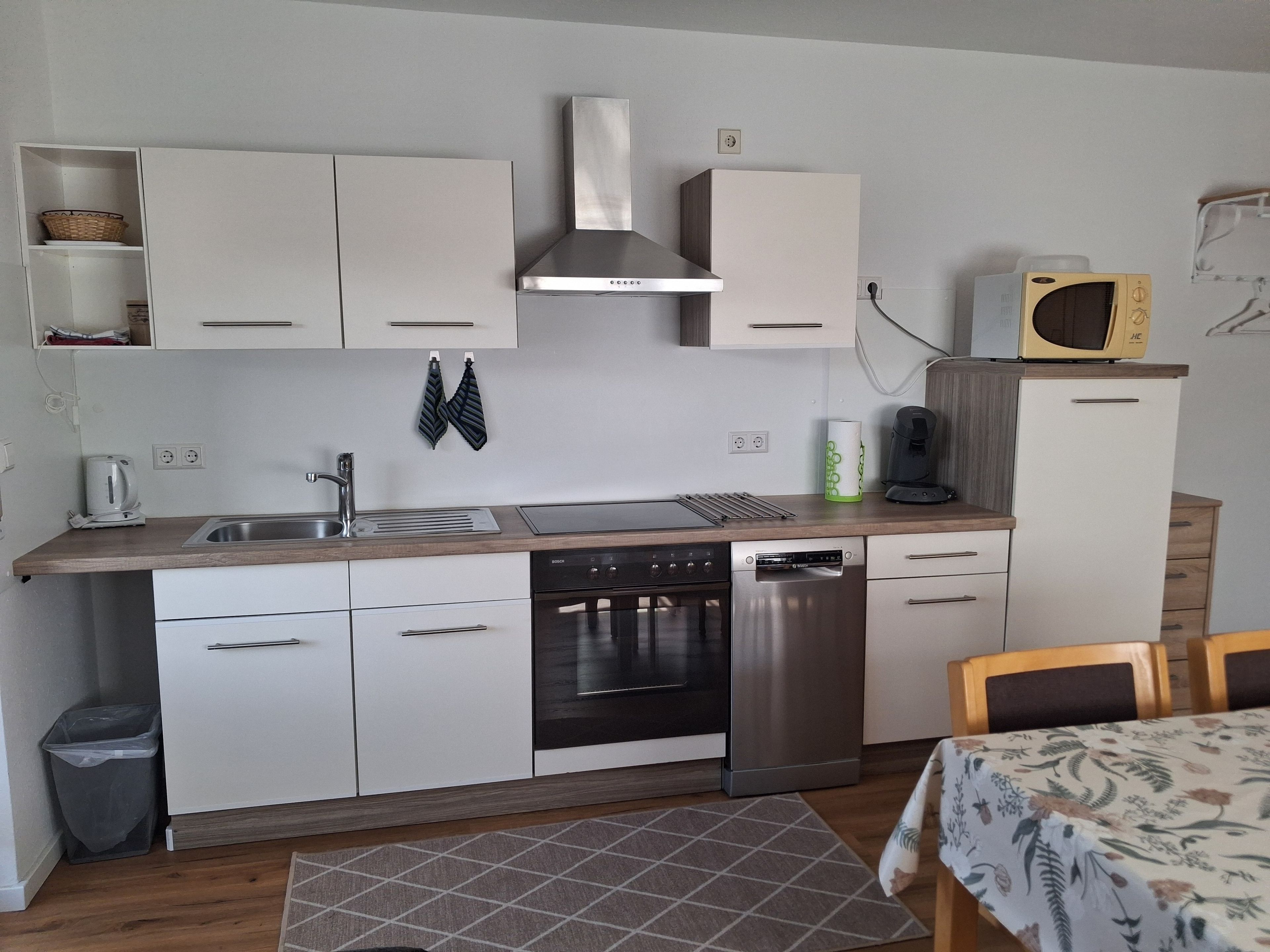 Uma cozinha compacta com armários brancos, coifa de aço inoxidável, micro-ondas e lava-louças.
