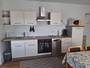 A compact kitchen with white cabinets, a stainless steel range hood, a microwave, and a dishwasher.