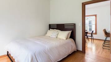 A bedroom with a wooden bed, white bedding, and a wooden floor.
