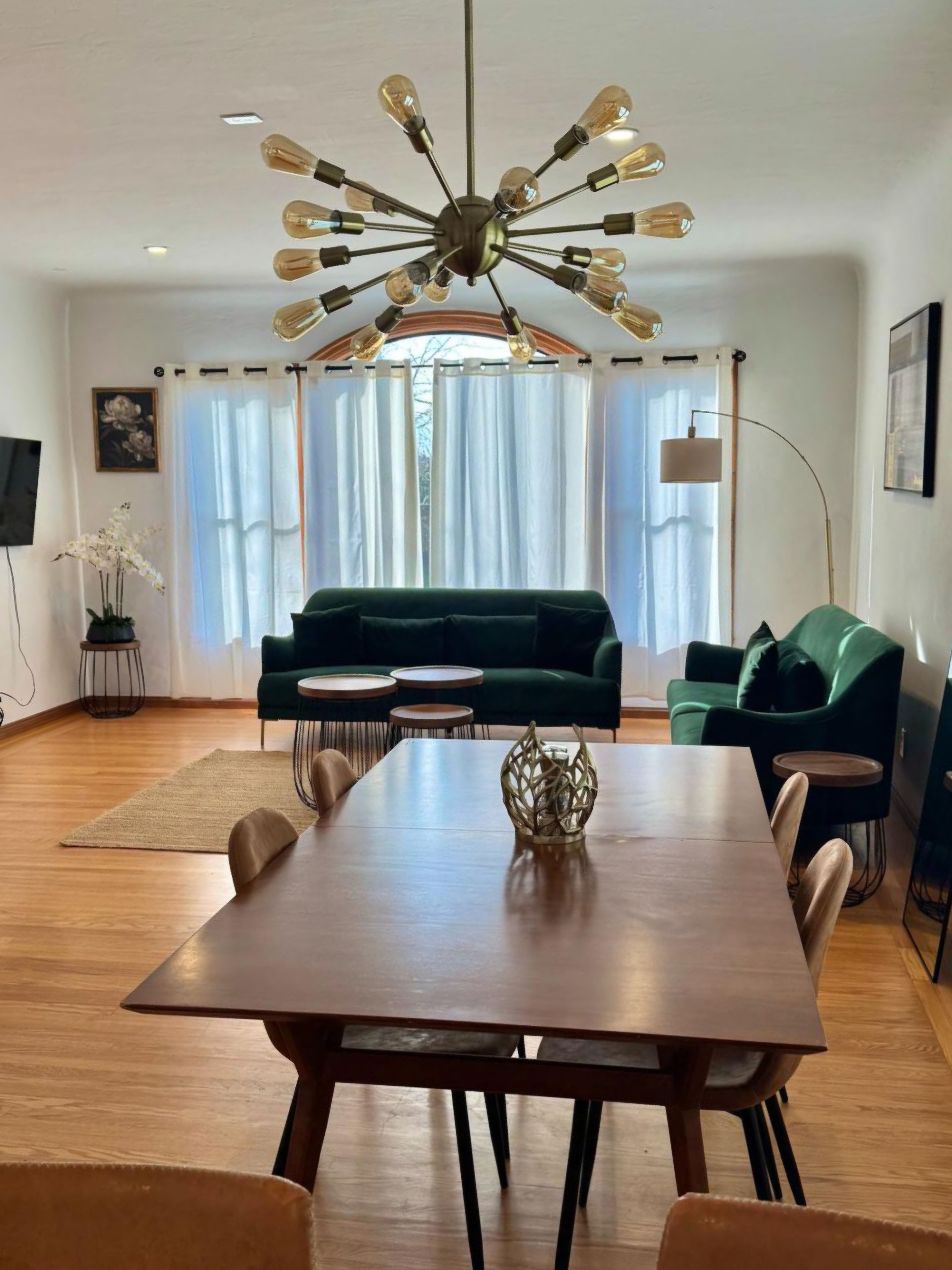 A modern living room with a dining table, green sofas, and a unique ceiling light fixture.