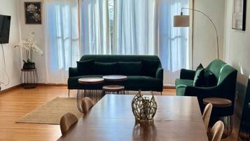 A modern living room with a dining table, green sofas, and a unique ceiling light fixture.