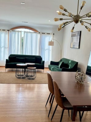 A modern living room with a green sofa, a dining table with chairs, and a unique ceiling light fixture. - Stunning Two Bedroom Mediterranean Home (Oakland)