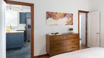 Ein Schlafzimmer mit einem Holzkasten, einem Bett und einer durch eine offene Tür einsehbarer Küche.