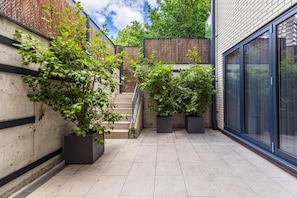 A courtyard with a staircase, potted plants, and a building with large windows. - Aldgate East by Excel Apartments (London)