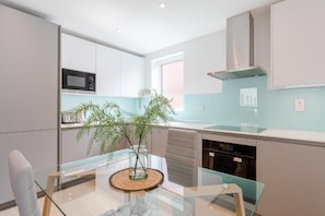A modern kitchen with a glass dining table, a microwave, and a plant. - Aldgate East by Excel Apartments (London)