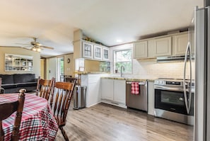 A kitchen with wooden cabinets, a stainless steel refrigerator, and a dining area with a table and chairs. - Tango Spring (Cranberry Township)