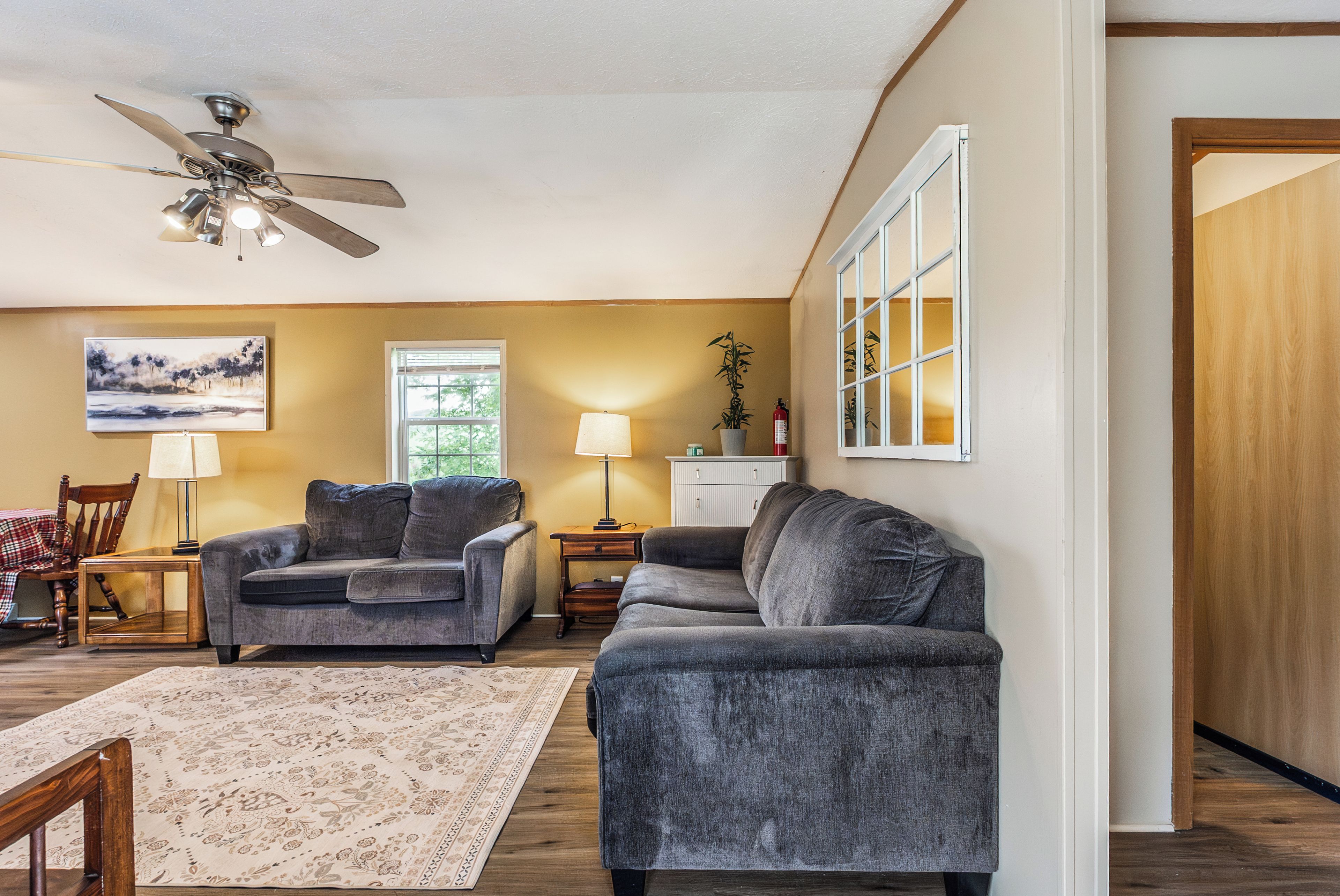A living room with two sofas, a wooden coffee table, a floor lamp, a painting on the wall, and a ceiling fan.