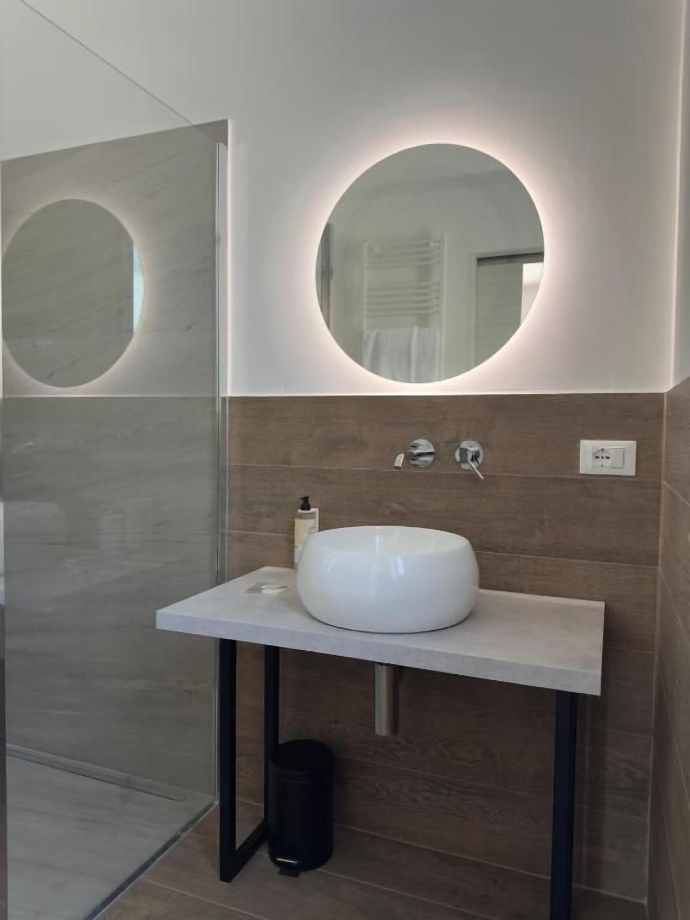Un baño con un lavamanos blanco, un espejo redondo y un perchero para toallas.