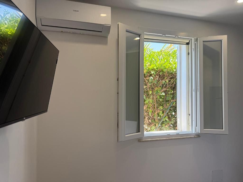 A room with a white wall, a window with white shutters, and an air conditioning unit.